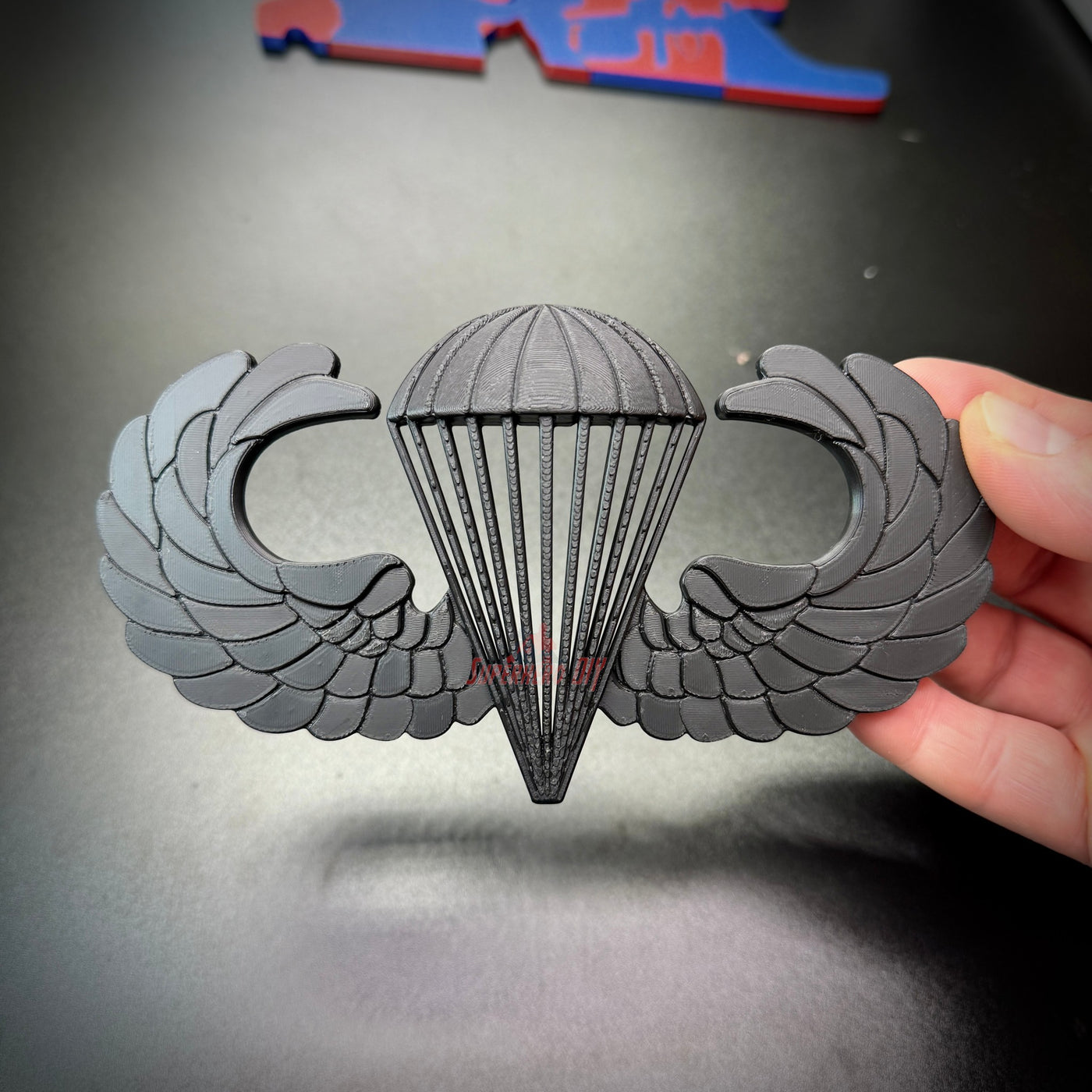 Airborne jump wings badge with black wings and parachute design held in hand, symbolizing military achievement.