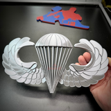 Airborne jump wings badge replica with silver finish, held in hand, symbolizing paratrooper achievement.