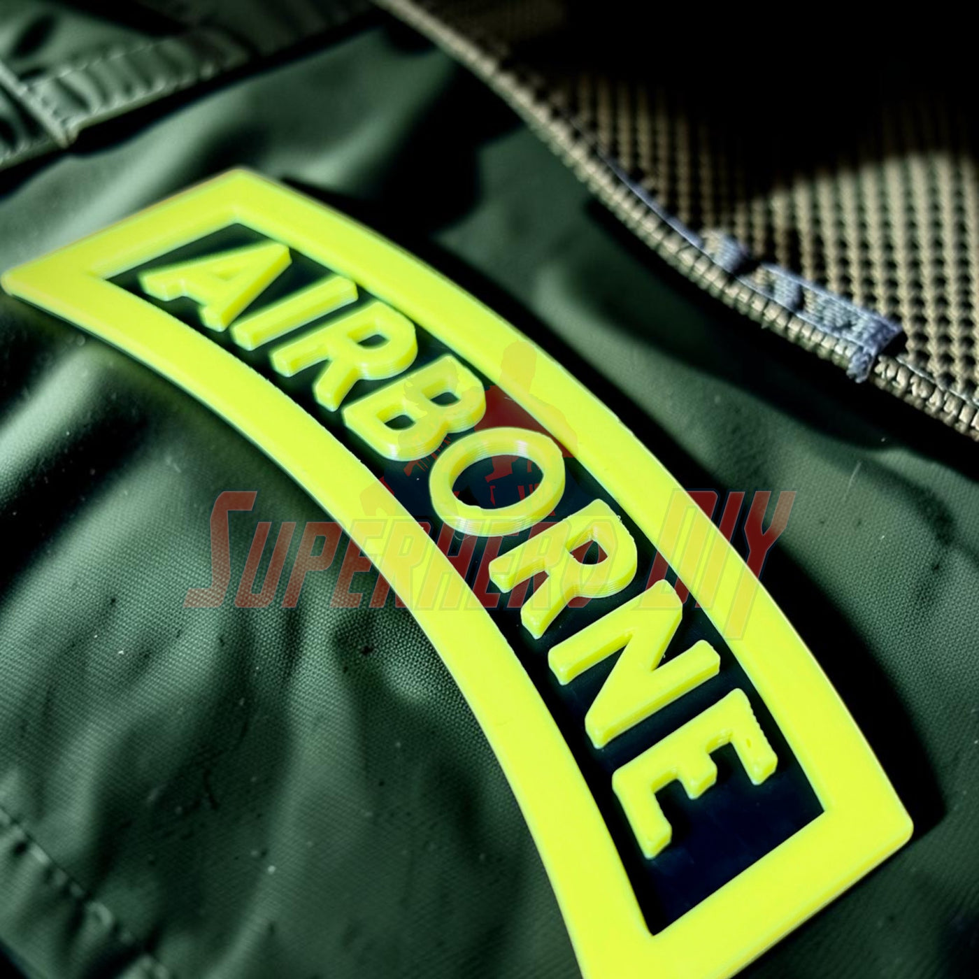 3D airborne tab displayed on green fabric with bold yellow lettering and black outline.