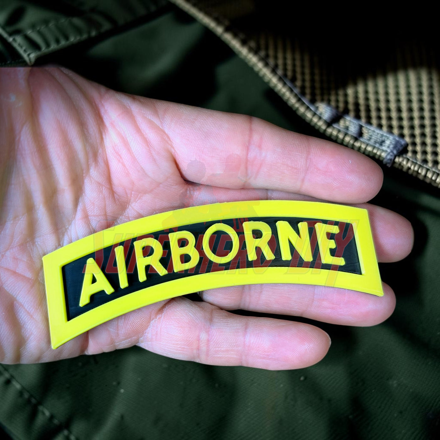 3D airborne tab displayed in a hand, featuring bold yellow lettering on a black background.