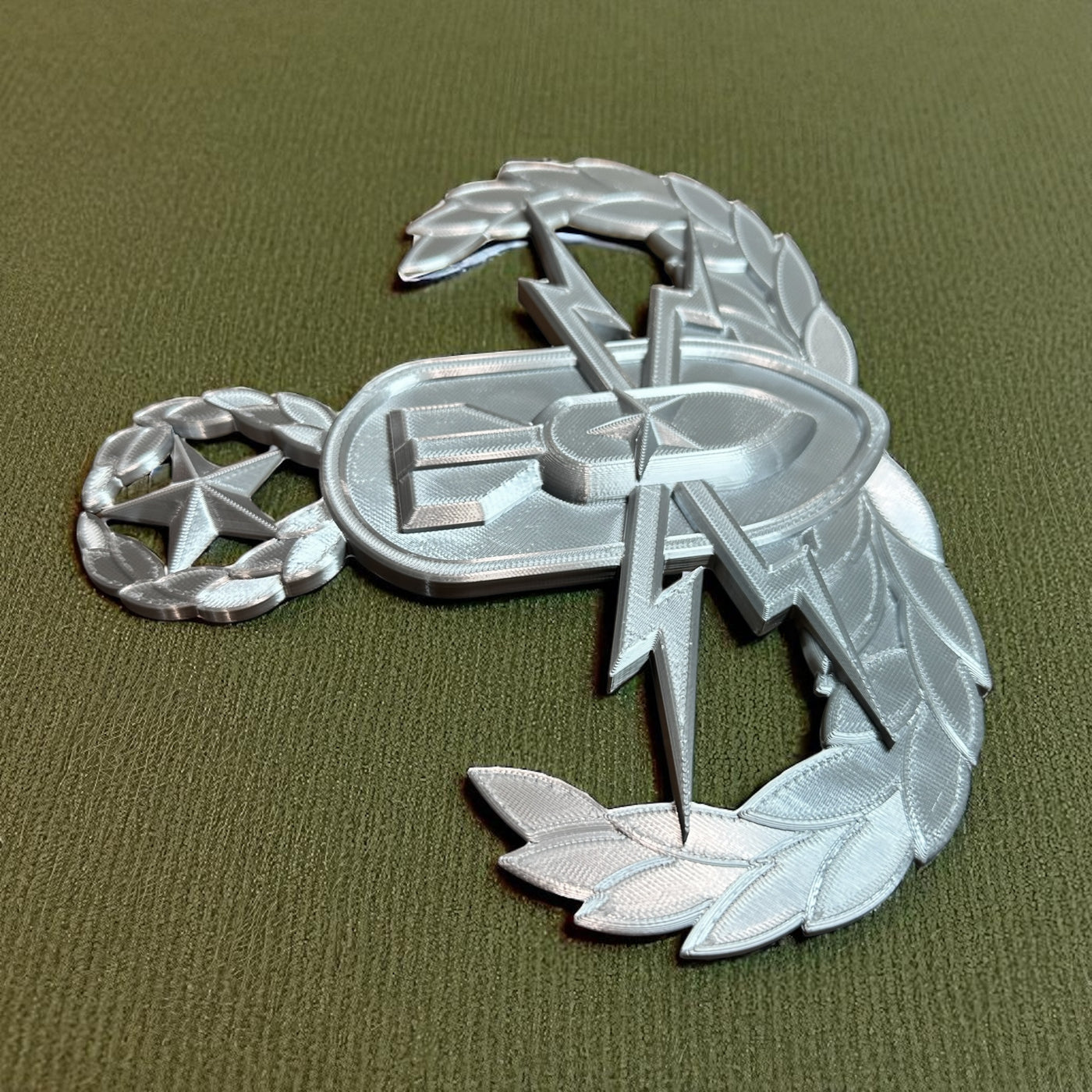 Replica EOD Badge Display in silver, showcasing intricate design on green background, symbolizing military technical skill.