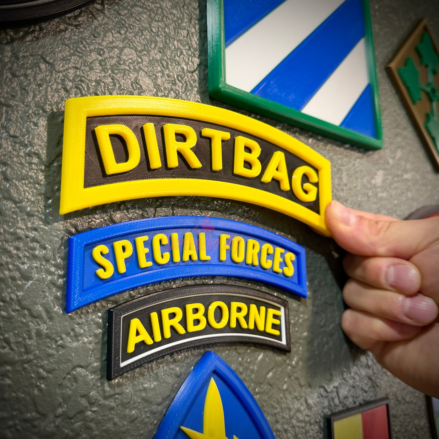 DIRTBAG tab displayed on a wall among other military patches, capturing a gag gift for soldiers.