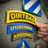 DIRTBAG tab displayed on a wall among other military patches, capturing a gag gift for soldiers.