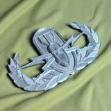 Replica EOD Badge Display on green fabric, symbolizing technical skill and honor across military branches.
