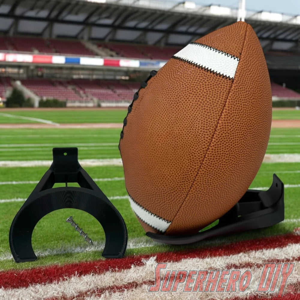 Black wall mount holder securely cradling a brown football with white stripes on a football field background. - SuperheroDIY