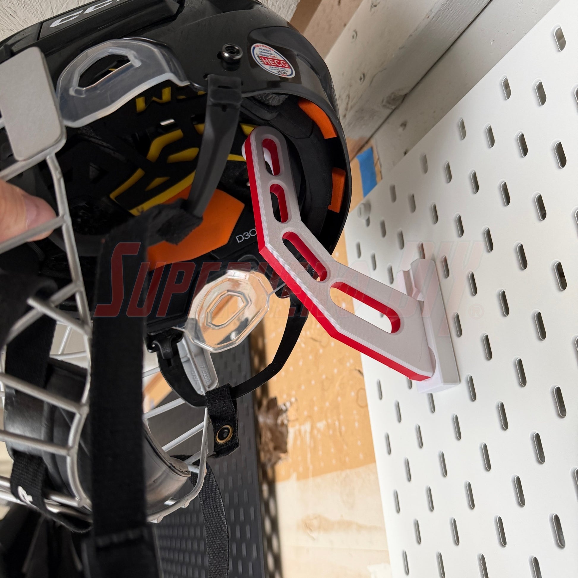Close-up of a hockey helmet with a red and white bracket attached, on a IKEA Skadis pegboard background.