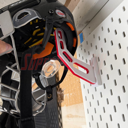 Close-up of a hockey helmet with a red and white bracket attached, on a IKEA Skadis pegboard background.