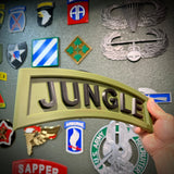 3D Jungle Tab display piece in army green with bold black lettering, held in hand against a backdrop of military patches.