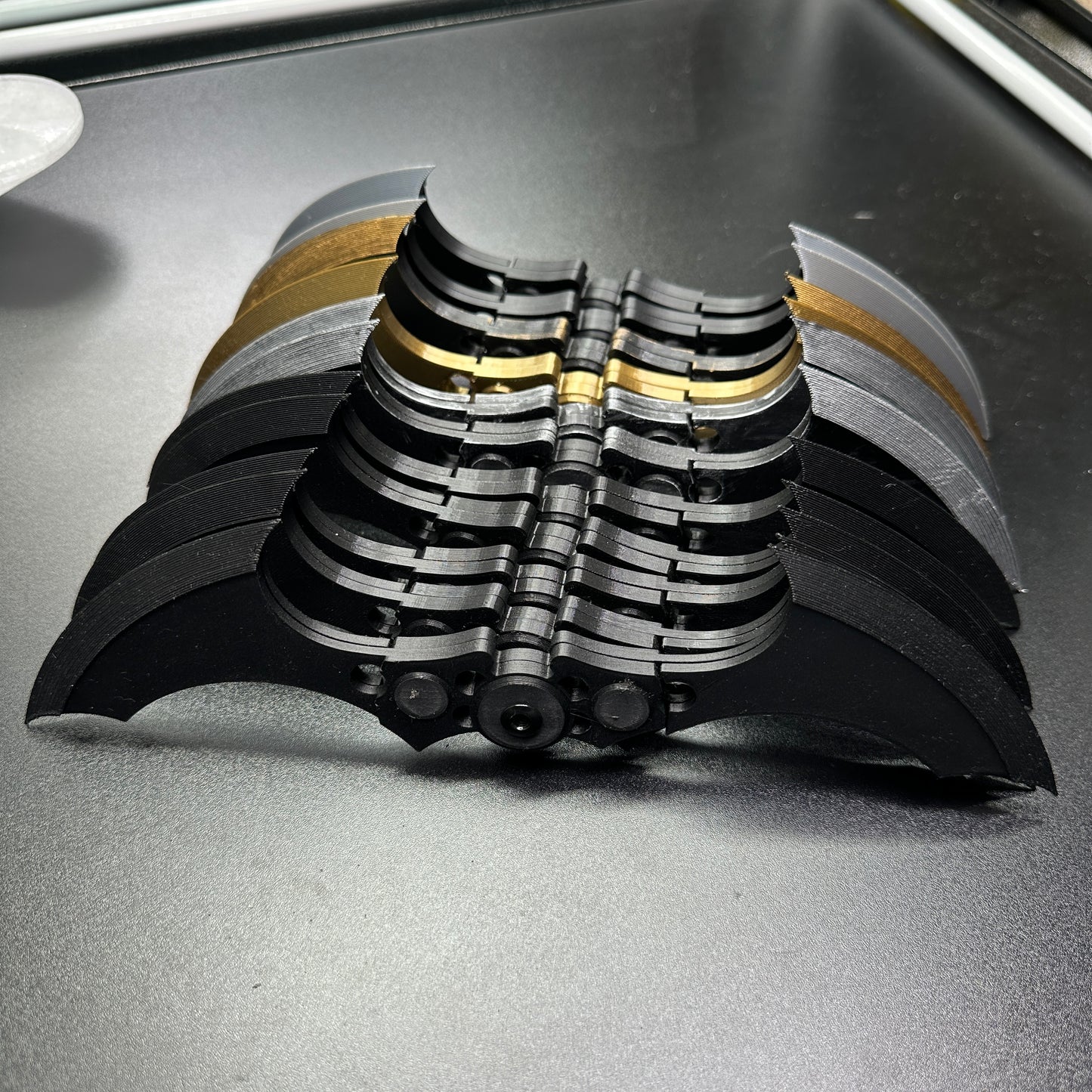 Display of MAGNETIC Folding Arkham Batarang Cosplay Prop - 10" version, showing multiple folded black metal Batarangs on a table.