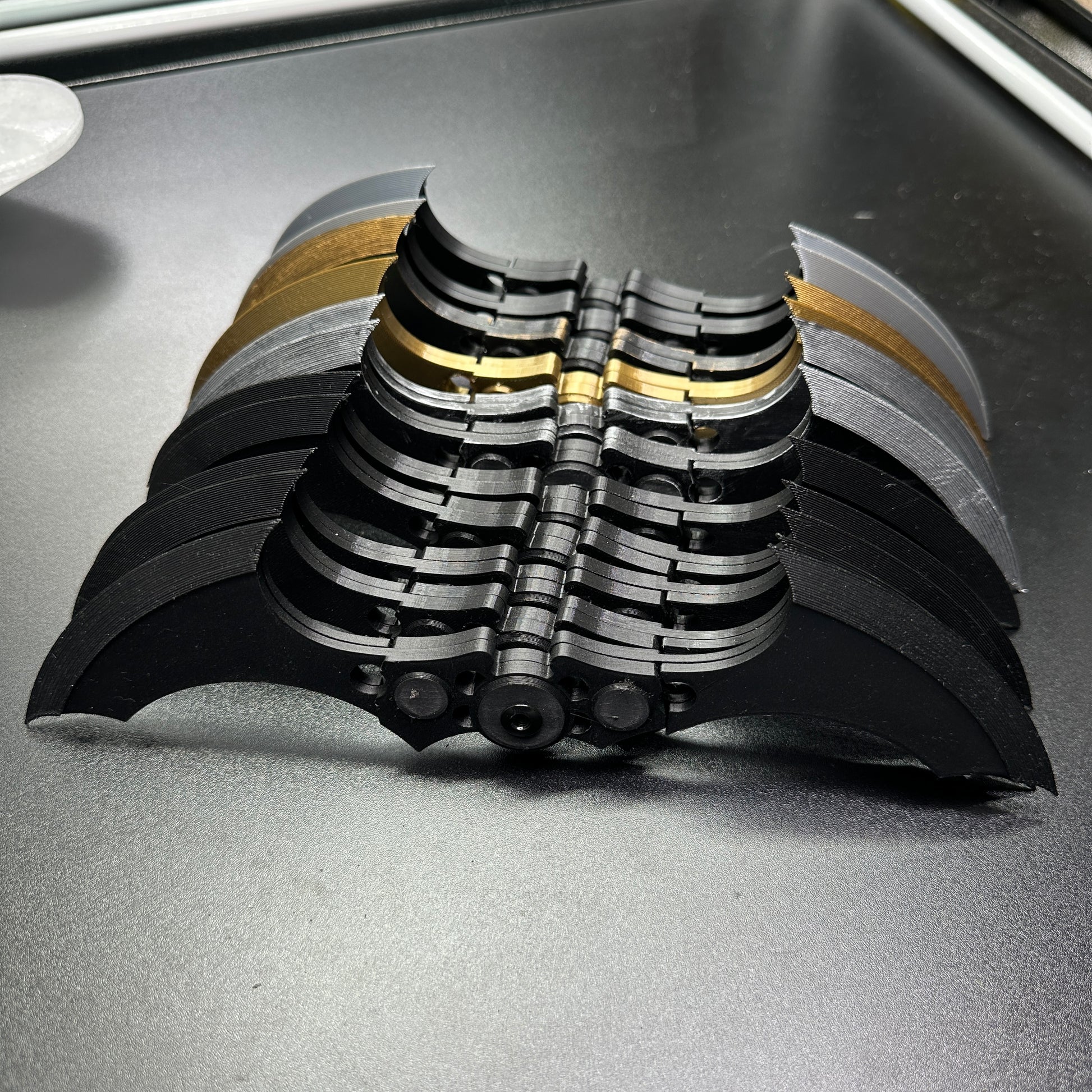 Display of MAGNETIC Folding Arkham Batarang Cosplay Prop - 10" version, showing multiple folded black metal Batarangs on a table.