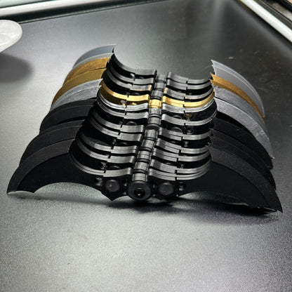 Display of MAGNETIC Folding Arkham Batarang Cosplay Prop - 10" version, showing multiple folded black metal Batarangs on a table.