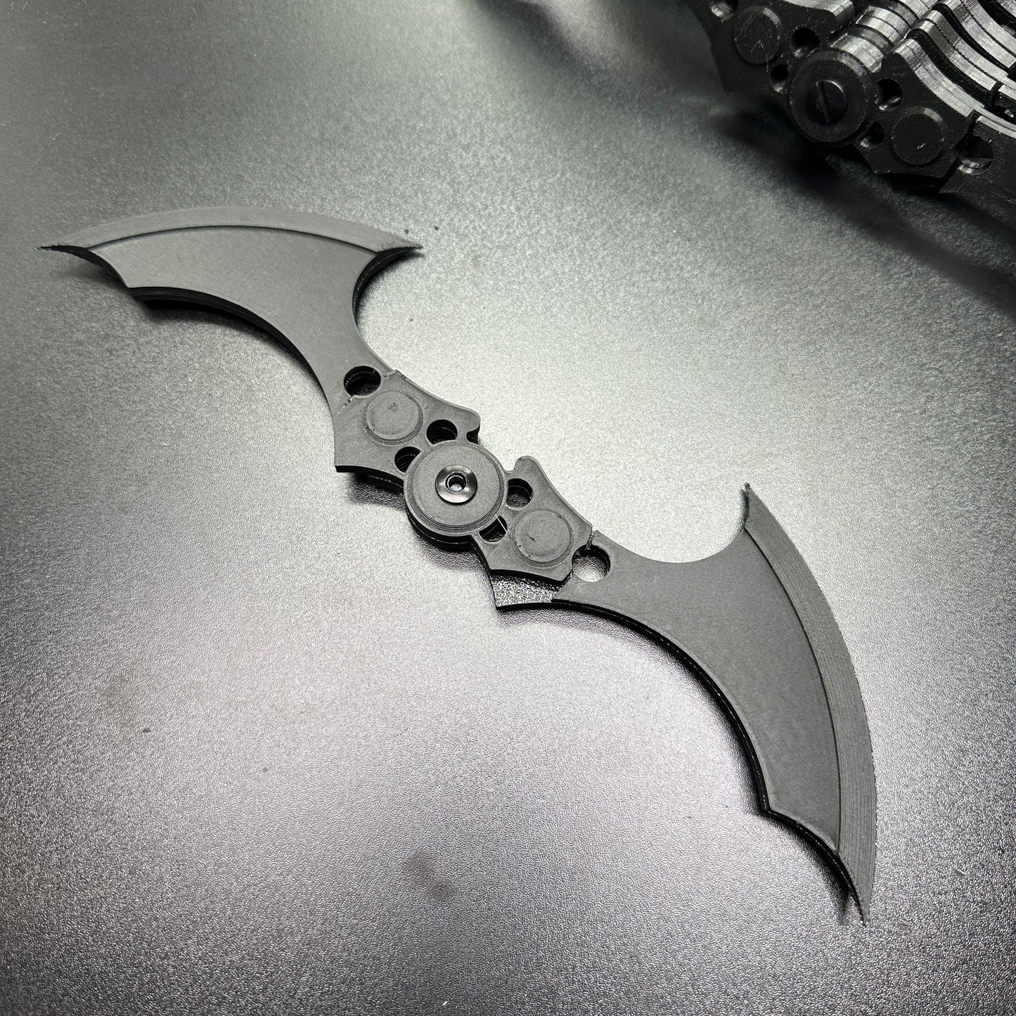 Close-up of MAGNETIC Folding Arkham Batarang Cosplay Prop - 10" version on dark surface, showcasing open position and sharp design.