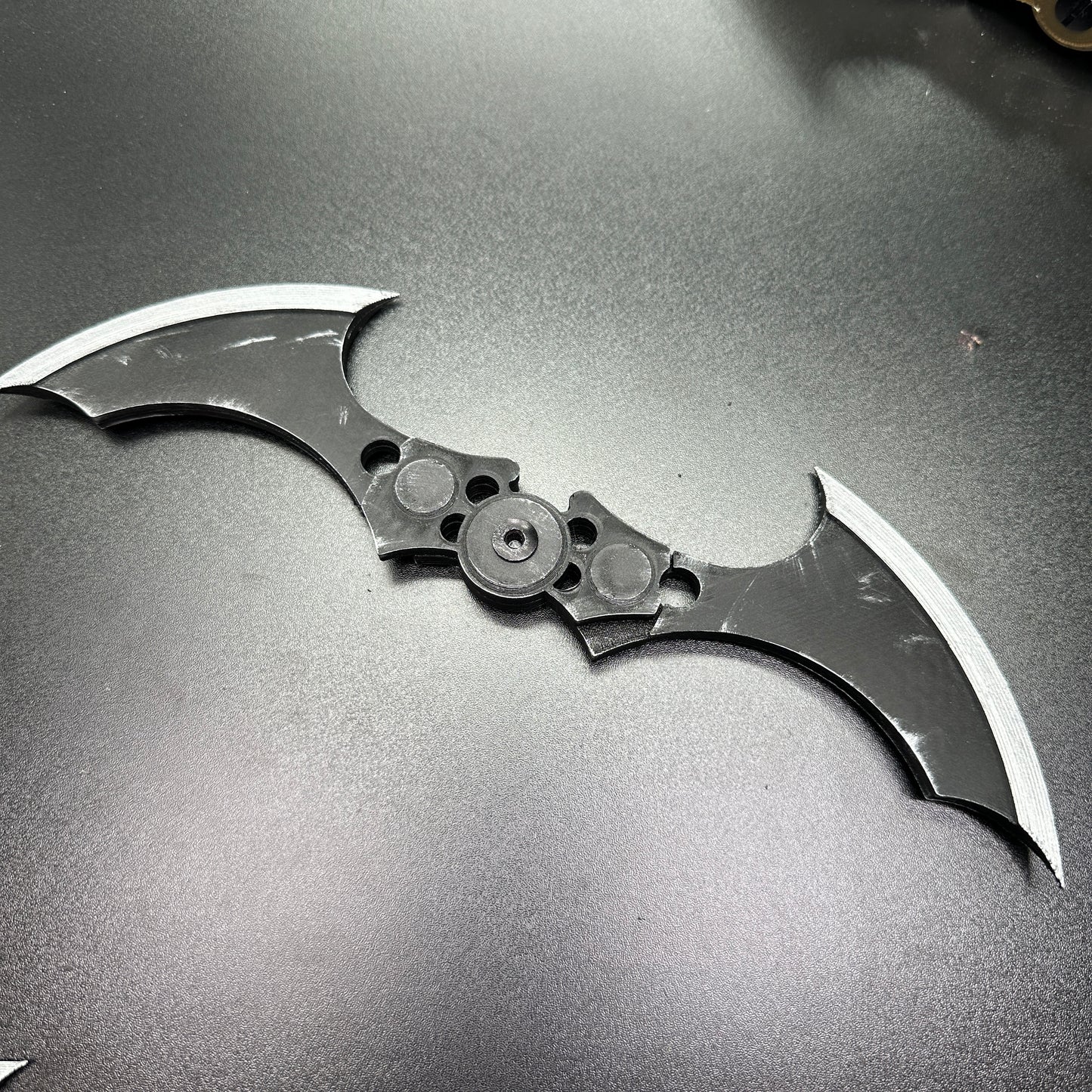 MAGNETIC Folding Arkham Batarang Cosplay Prop - 10" version, laying open on a dark surface, showcasing its dual blades and central hinge.