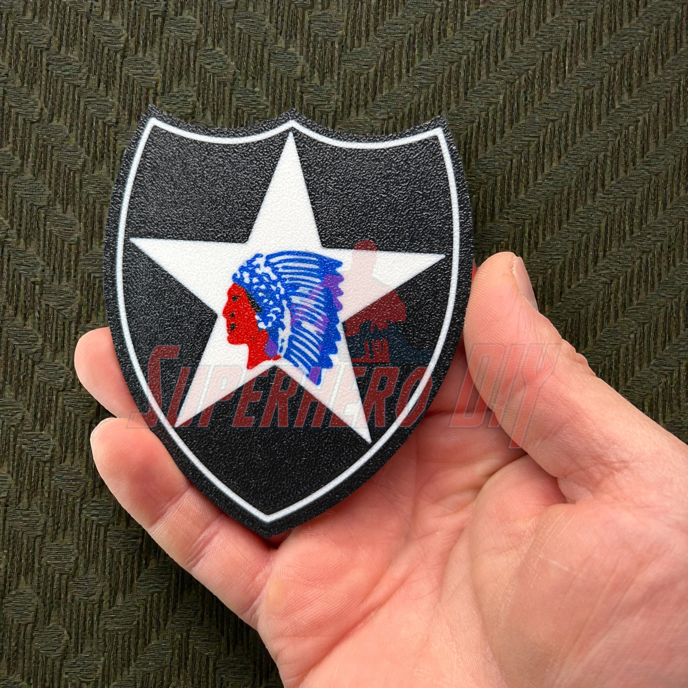 Hand holding a 3D-printed 2nd Infantry Division display insignia patch showcasing a star and Native American head.