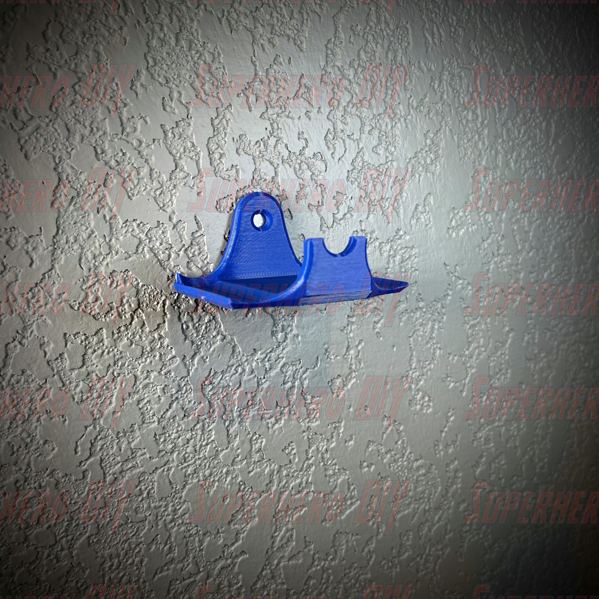 Blue PS4 controller wall mount for DualShock controllers attached to a textured wall, shown with a Command Strip for easy installation.