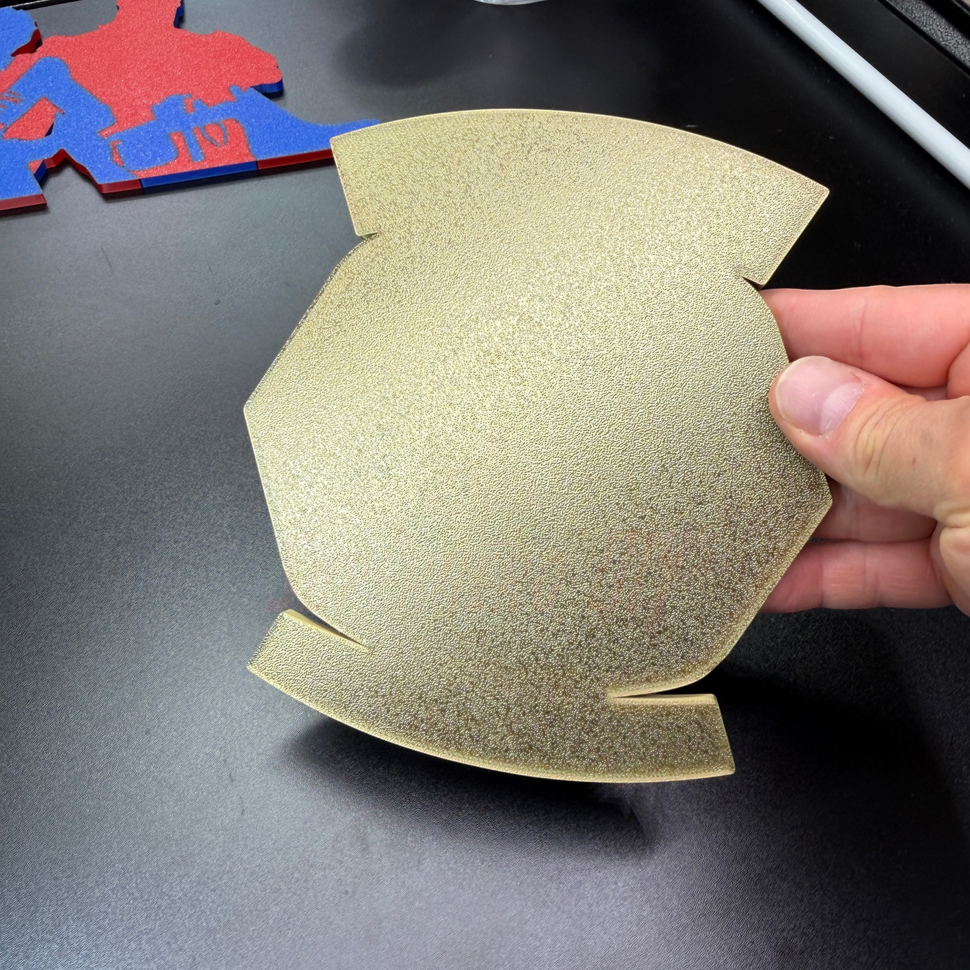 Hand holding a gold 3D display base for the Bradley Master Gunner Badge display, showcasing its unique design.