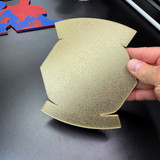 Hand holding a gold 3D display base for the Bradley Master Gunner Badge display, showcasing its unique design.