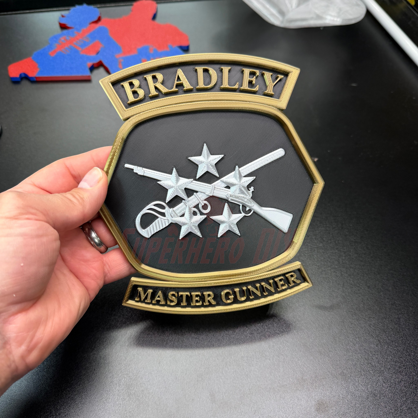 Bradley Master Gunner Badge display showing 3D insignia with crossed weapons and stars, perfect for desk or wall.