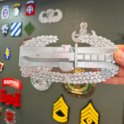 Combat Action Badge display insignia with bayonet and oak wreath held in hand, showcasing its detailed design.