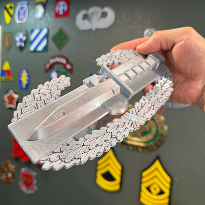 Combat Action Badge display insignia held in hand, showcasing bayonet and oak wreath design.