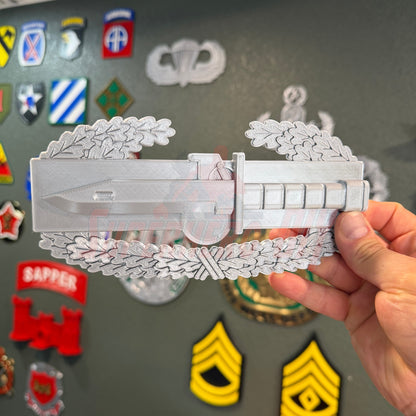 Combat Action Badge Display Insignia replica held by a hand, showcasing bayonet and oak wreath detail.