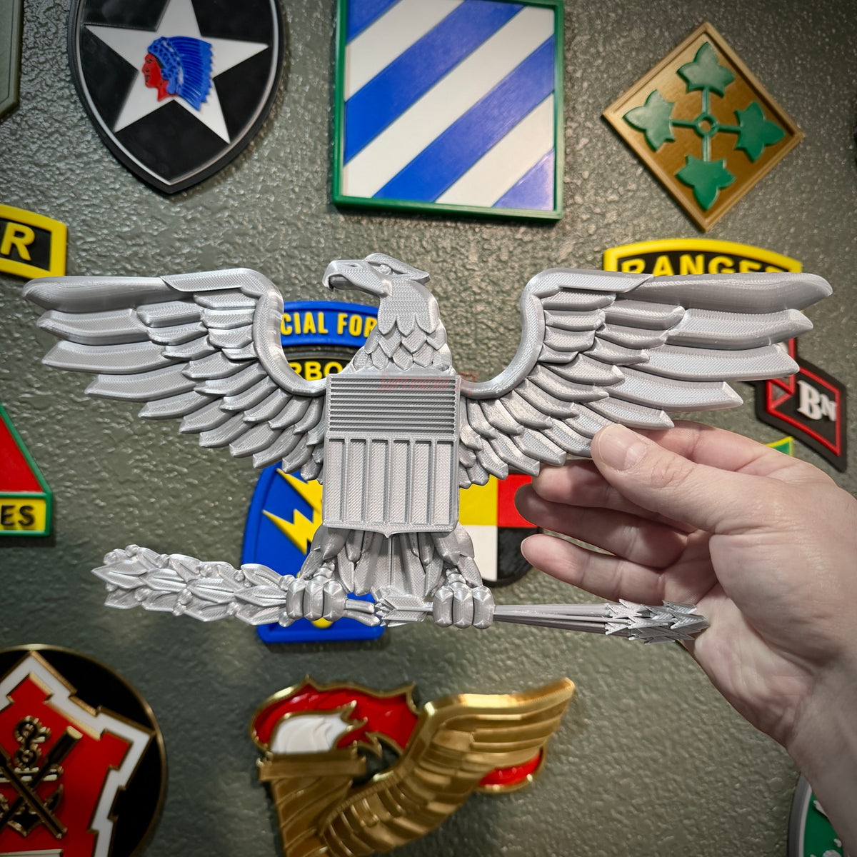 Hand holding a detailed Colonel Captain rank insignia O-6 eagle emblem against a background of military patches.