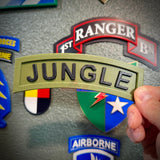Hand holding a 3D Jungle Tab display piece with army green background and black JUNGLE lettering.