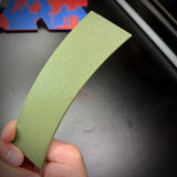 Hand holding a curved army green wall display piece resembling a jungle tab.