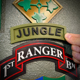 Image of a hand holding a jungle tab in army green with black lettering on a textured wall.