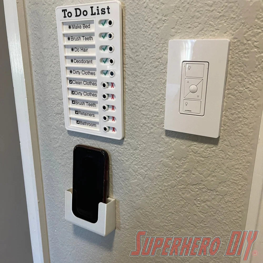 Wall-mounted phone holder under a to-do list on a bathroom wall, installed with Command strips for easy mounting.