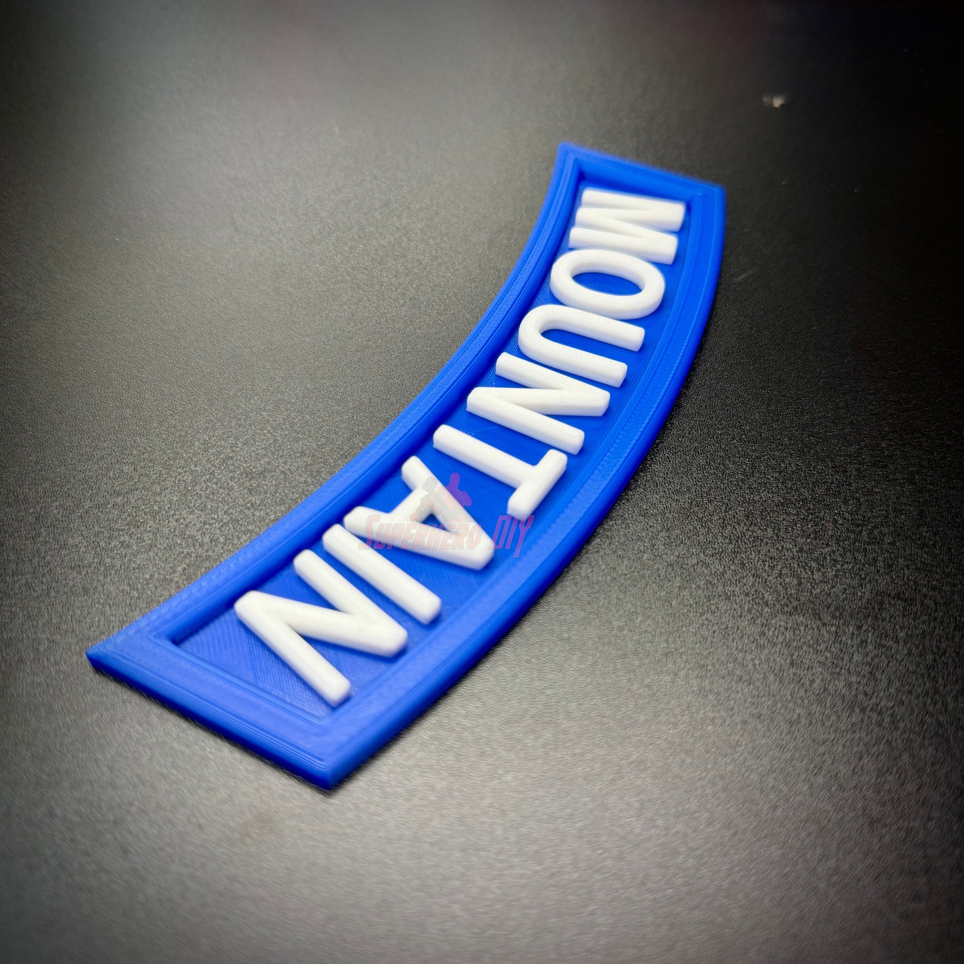 3D mountain tab wall display in blue with raised white lettering on a black surface.