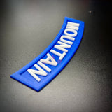 3D mountain tab wall display in blue with raised white lettering on a black surface.