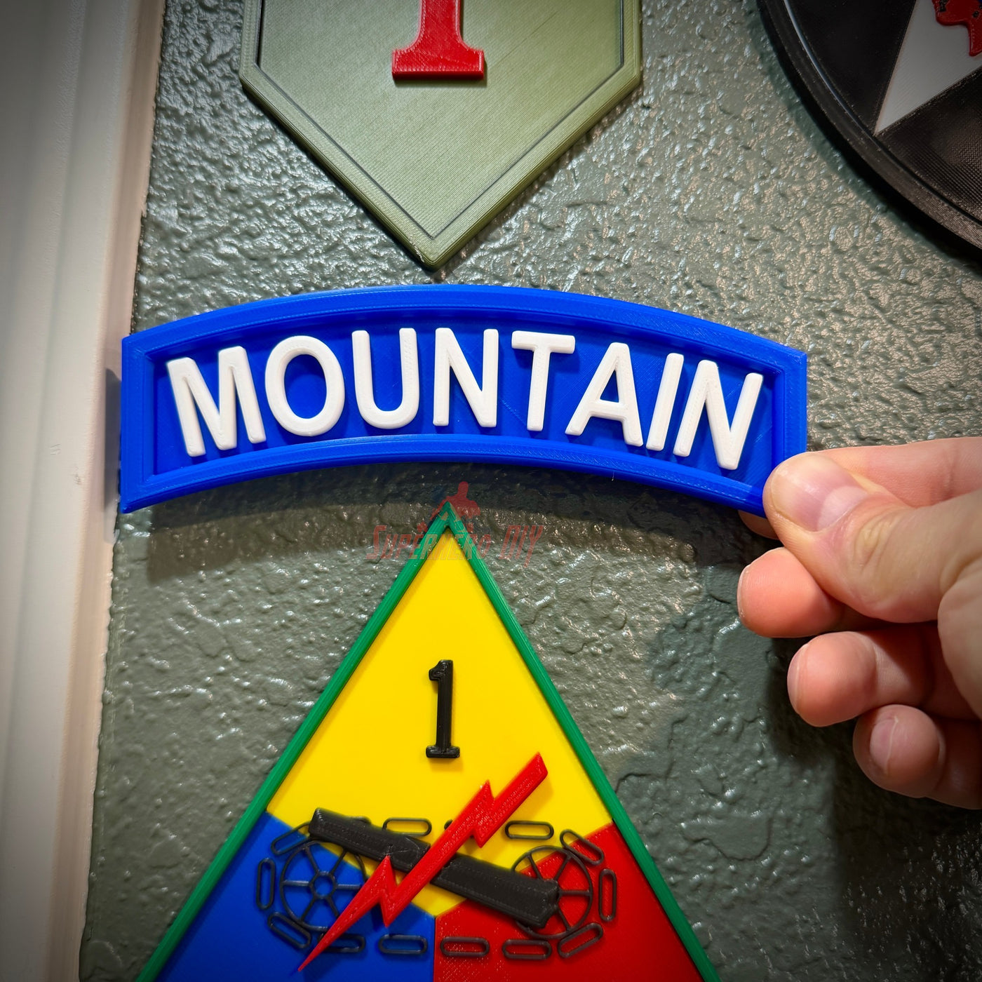 3D mountain tab wall display with raised white lettering and deep blue background held against a textured wall.