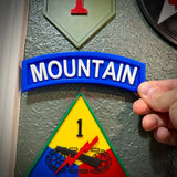 3D mountain tab wall display with raised white lettering and deep blue background held against a textured wall.