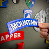 3D mountain tab wall display with raised white lettering against a blue background, held by a hand.