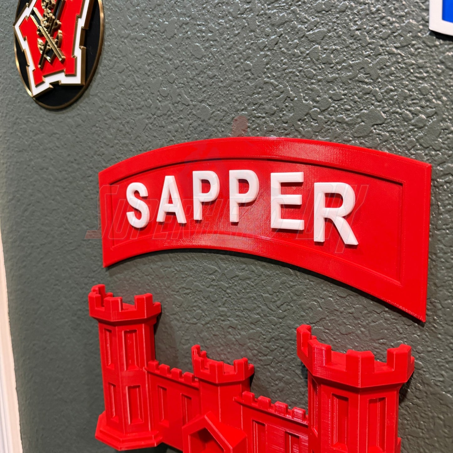 3D sapper tab display piece in red mounted on a wall, showcasing combat engineer insignia.