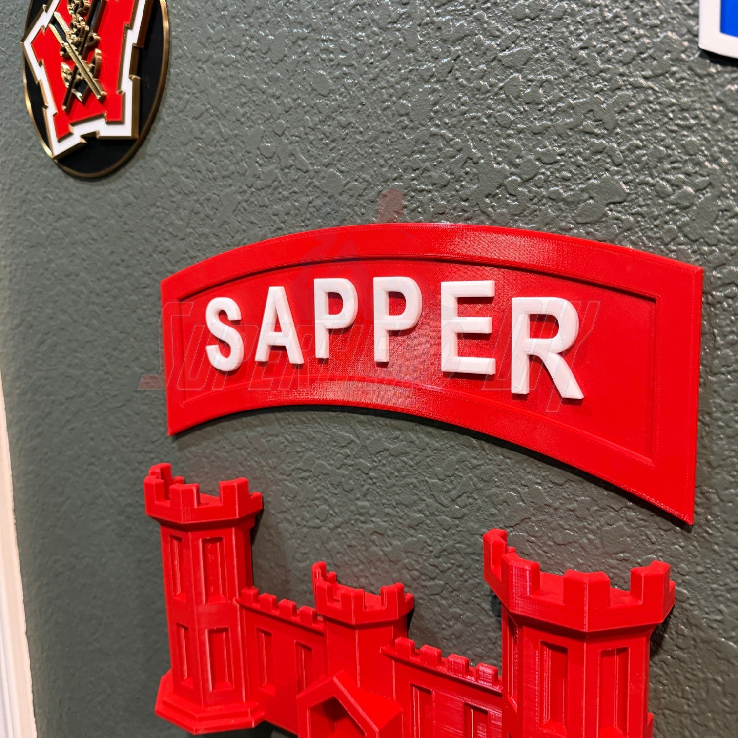 3D sapper tab display piece in red mounted on a wall, showcasing combat engineer insignia.