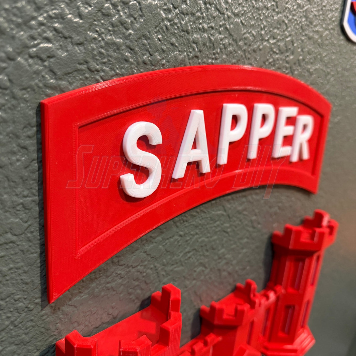 3D sapper tab display with bold red lettering on a gray surface, representing combat engineer achievement.