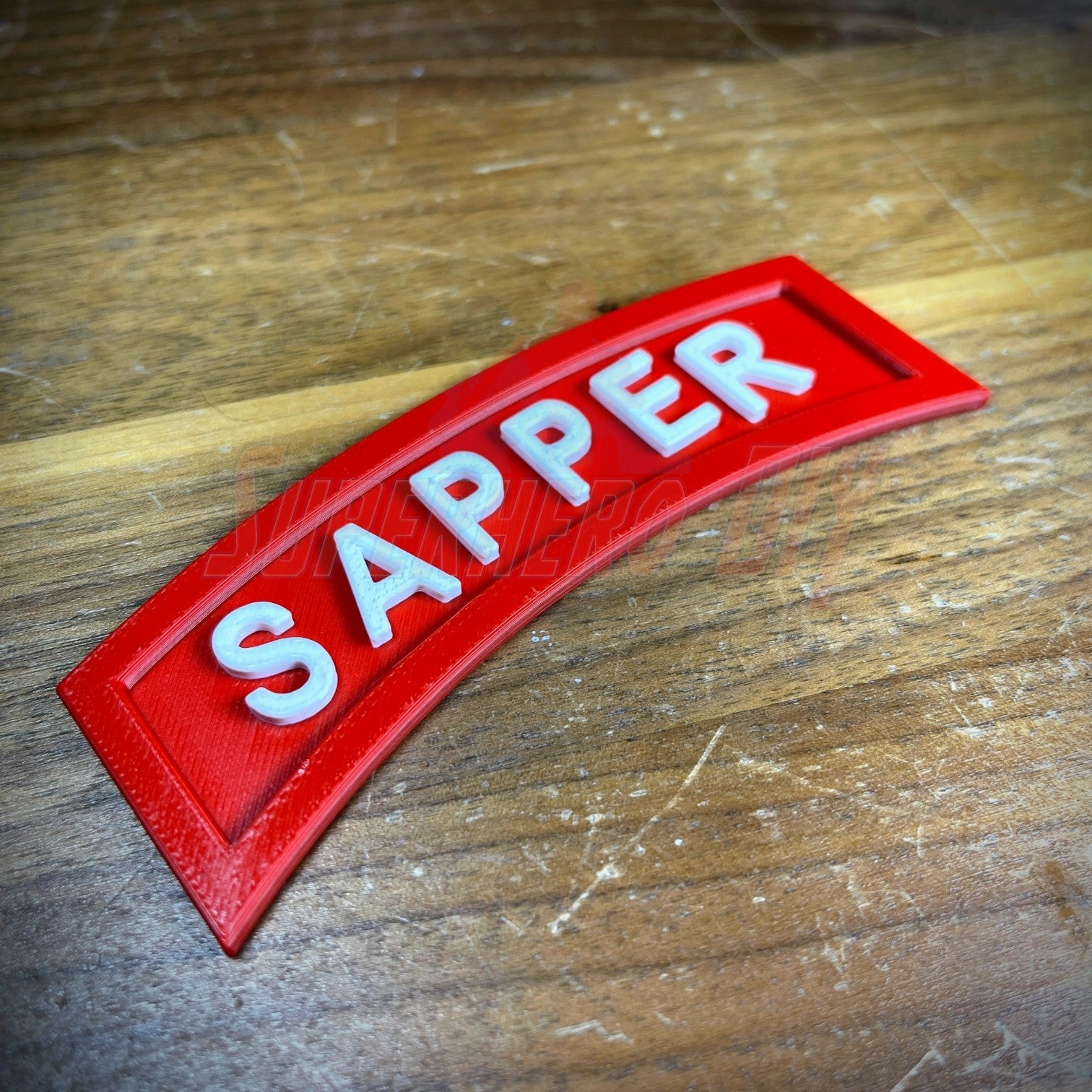 3D Sapper Tab in red with white lettering on a wooden surface, showcasing combat engineer achievement.