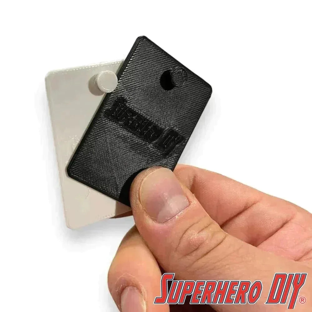 Close-up of a hand holding a blister pack wall hanger, featuring a discreet design for mounting collectible action figures without wall damage.