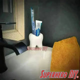 Tooth shaped bathroom organizer holding toothbrush and toothpaste placed on a modern sink with a yellow towel beside it.