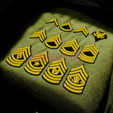 Multiple Army enlisted rank insignia patches in yellow displayed on a textured surface.