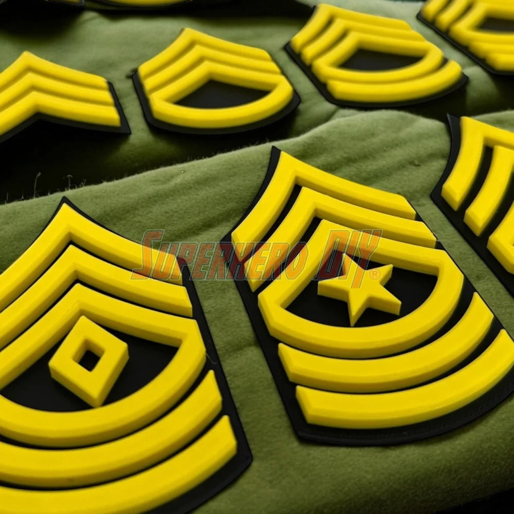 Close-up of bold, 3D-printed Army enlisted rank insignia displayed in multiple sizes on a green fabric.