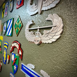 Air Assault Badge display mounted on wall among various military insignia and badges.
