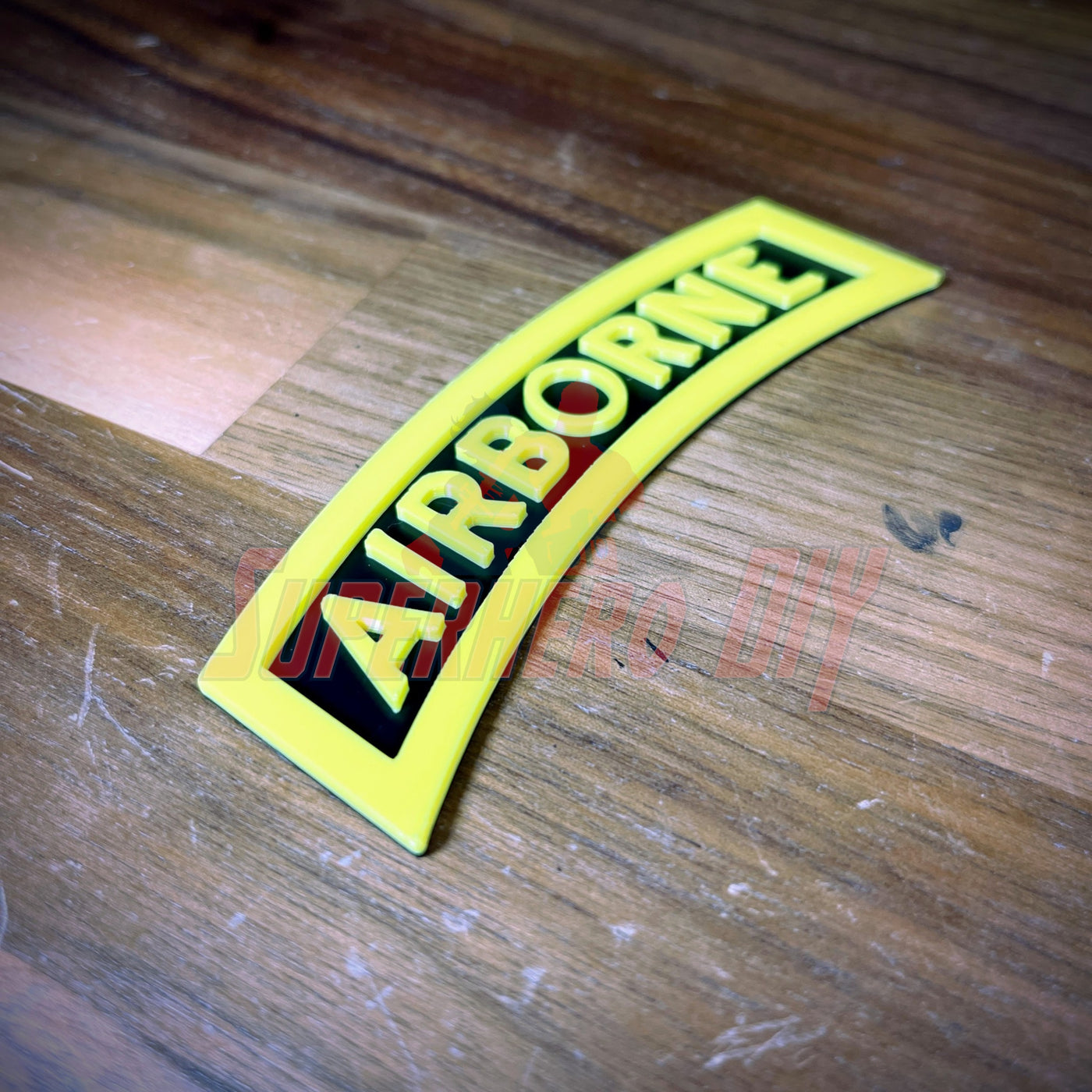 3D airborne tab displayed on a wooden surface, featuring bold yellow lettering on a black background.