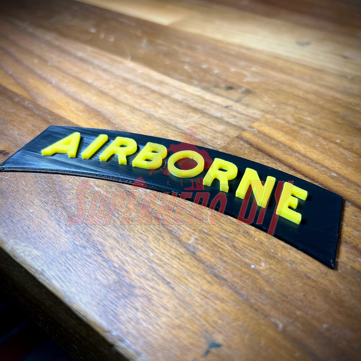 3D airborne tab displayed on a wooden surface, featuring bold yellow lettering on a solid black background.