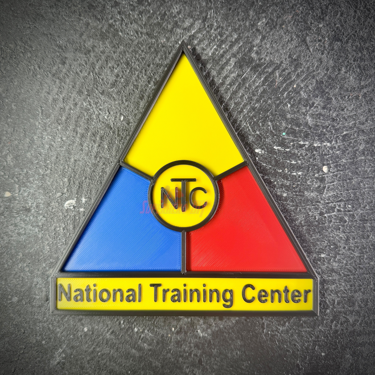 NTC insignia wall display shown straight on, yellow, blue, and red triangle with National Training Center banner