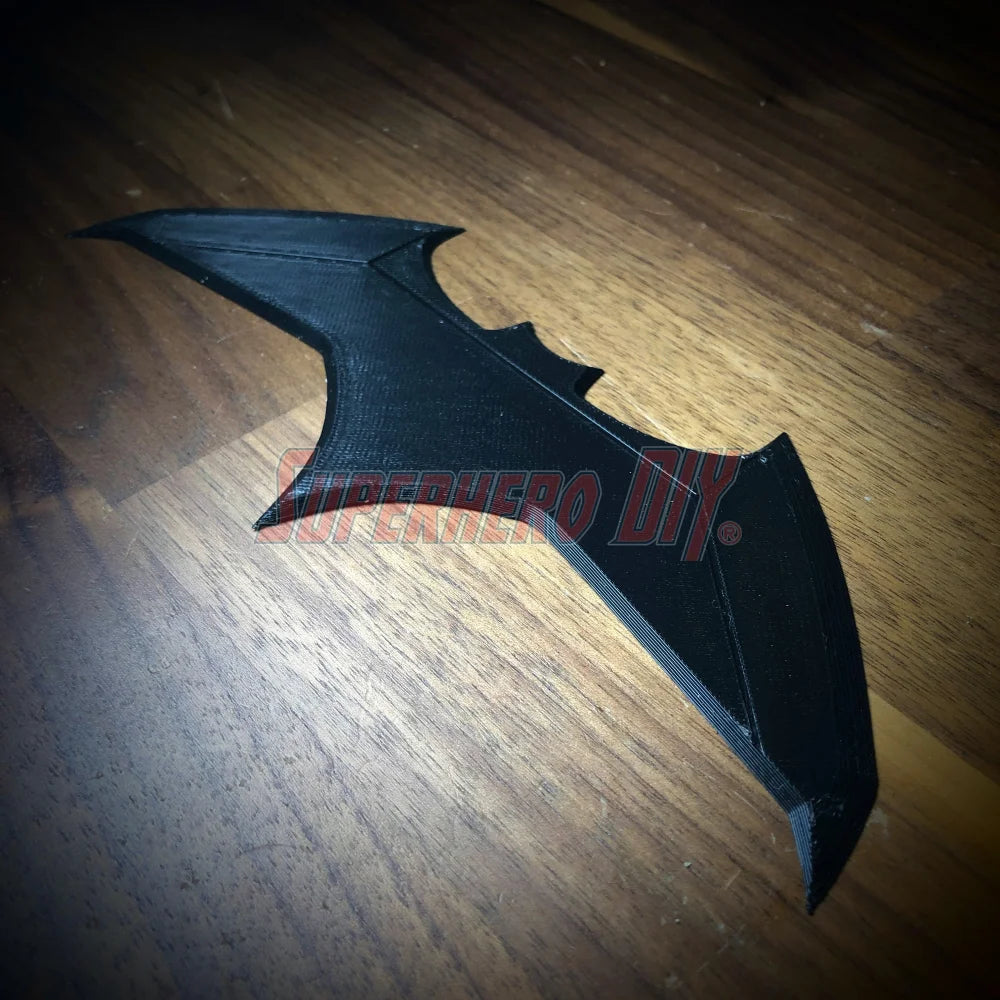 3D-printed BvS JL batarang prop in black plastic on wooden surface