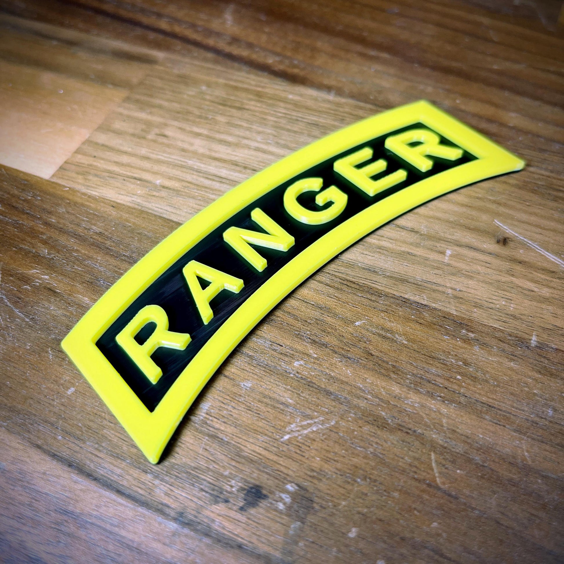 3D Army Ranger Tab replica in yellow-on-black design on a wooden surface, emphasizing its sharp detail and display quality.