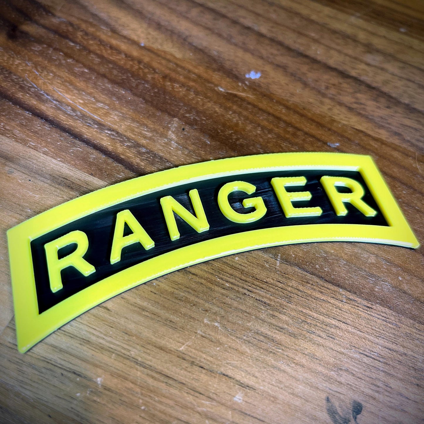 3D Army Ranger tab replica showing the iconic yellow-on-black design on a wooden surface.